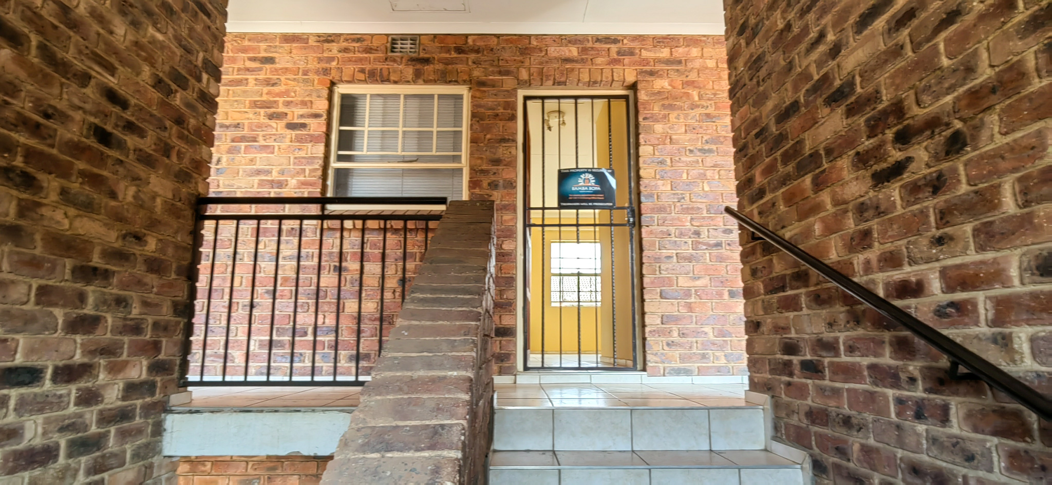 Brick stairwell entrance with metal railing and barred door at an apartment building