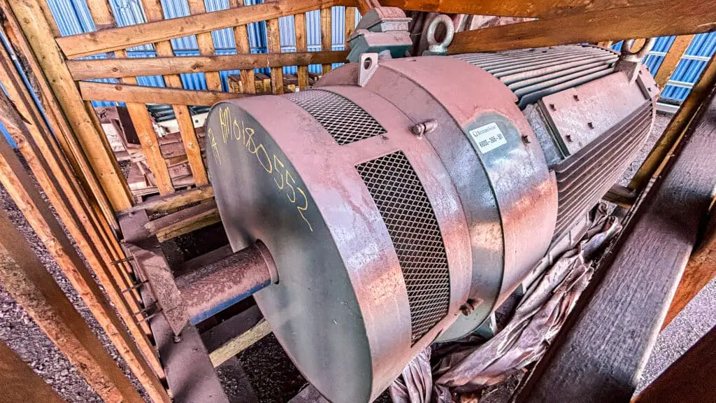 Large rusty industrial electric motor mounted in a wooden-framed storage area.